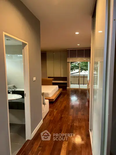 Modern bedroom with wooden flooring and balcony view, featuring sleek design and natural light.
