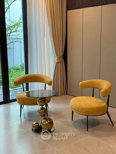 Stylish modern living room with unique chairs and glass table, floor-to-ceiling windows, and garden view.