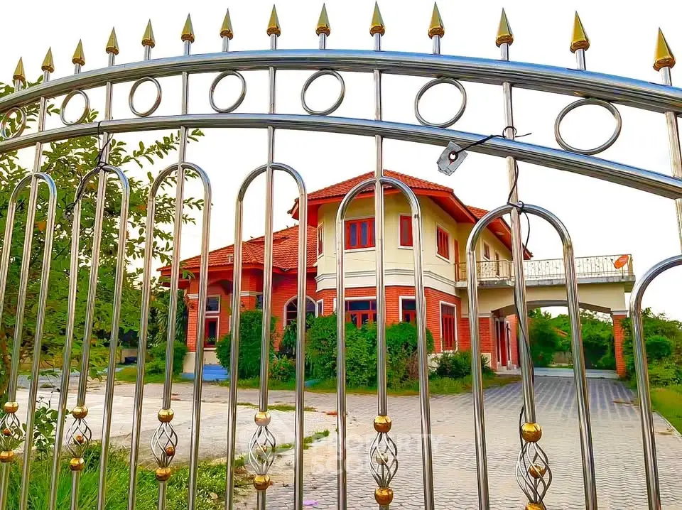 Charming two-story house with red accents and spacious driveway behind ornate metal gate.
