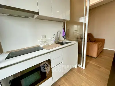 Modern kitchen with sleek appliances and cozy living area in open layout apartment.