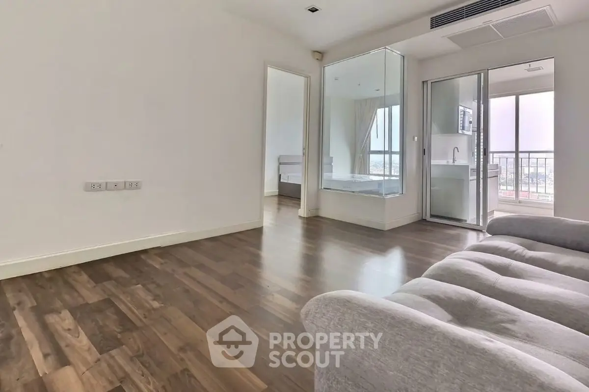Spacious modern living room with wooden flooring and glass-walled bathroom, featuring a cozy sofa and balcony view.