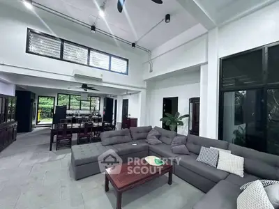 Spacious modern living room with high ceilings and large windows, featuring a cozy sectional sofa and elegant dining area.