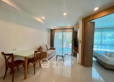 Modern open-plan living room with dining area and bedroom view, featuring sleek furniture and large windows.