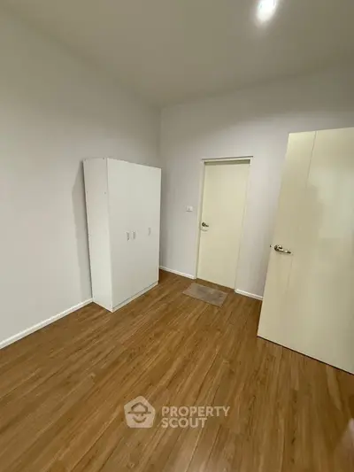 Spacious bedroom with wooden flooring and white wardrobe, perfect for modern living.