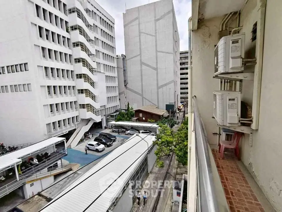 Urban view from balcony overlooking modern buildings and parking area.