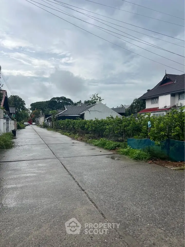 Charming residential street view with lush greenery and traditional houses under a cloudy sky.