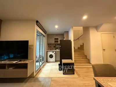 Modern living area with open kitchen and washing machine, featuring sleek design and cozy ambiance.