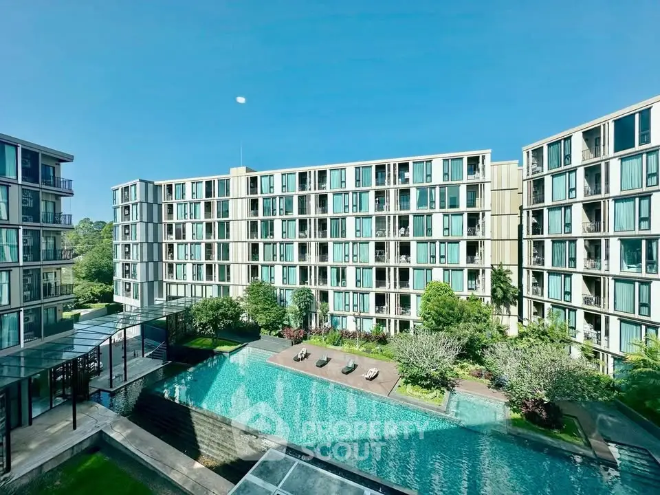 Modern apartment complex with pool and lush greenery under clear blue sky.