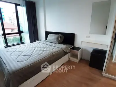 Modern bedroom with large window and stylish decor in urban apartment.