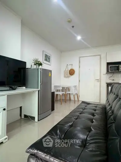 Modern living room with sleek black sofa, TV, and compact dining area in a cozy apartment.