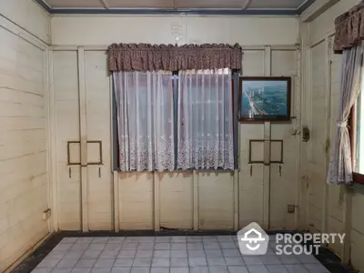 Vintage-style room with wooden walls and tiled floors, featuring lace curtains and a classic framed picture, exuding a quaint charm.