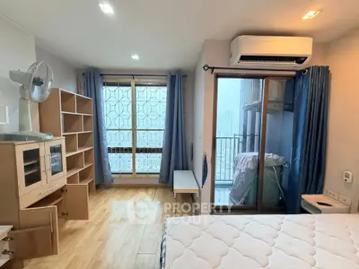 Bright bedroom with balcony access, featuring wooden flooring, modern furniture, and air conditioning.
