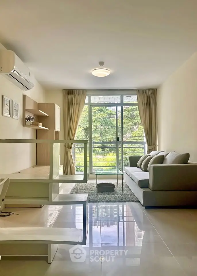 Modern living room with large windows and stylish decor, featuring a cozy sofa and lush greenery view.