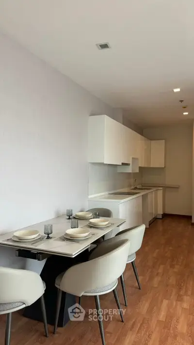 Modern kitchen with sleek white cabinets and dining area, featuring elegant tableware and wooden flooring.