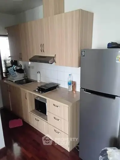 Modern kitchen with sleek wooden cabinets and stainless steel fridge in cozy apartment.