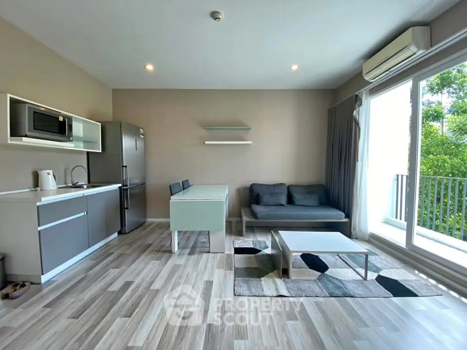 Modern open-plan living room with kitchen, featuring sleek furniture and large windows.