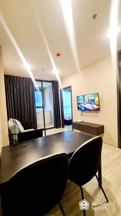 Modern living room with sleek furniture and wall-mounted TV, adjacent to a balcony with city view.