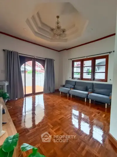 Spacious living room with elegant chandelier and polished wooden floors, featuring large windows for natural light.
