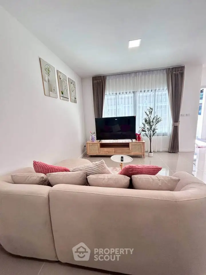 Modern living room with cozy sofa and large TV, bright natural light through curtains.
