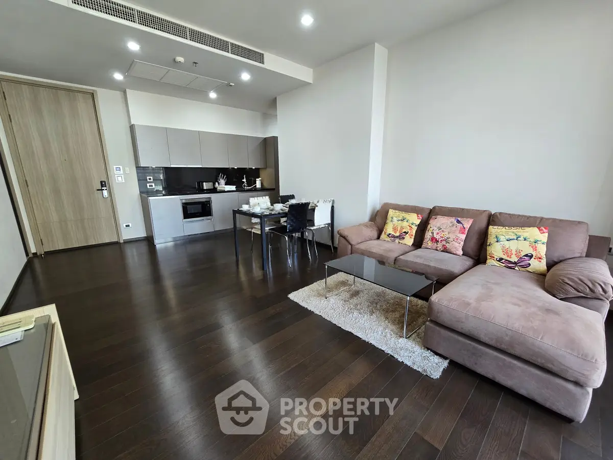 Modern living room with open kitchen, dark wood flooring, and stylish furniture.
