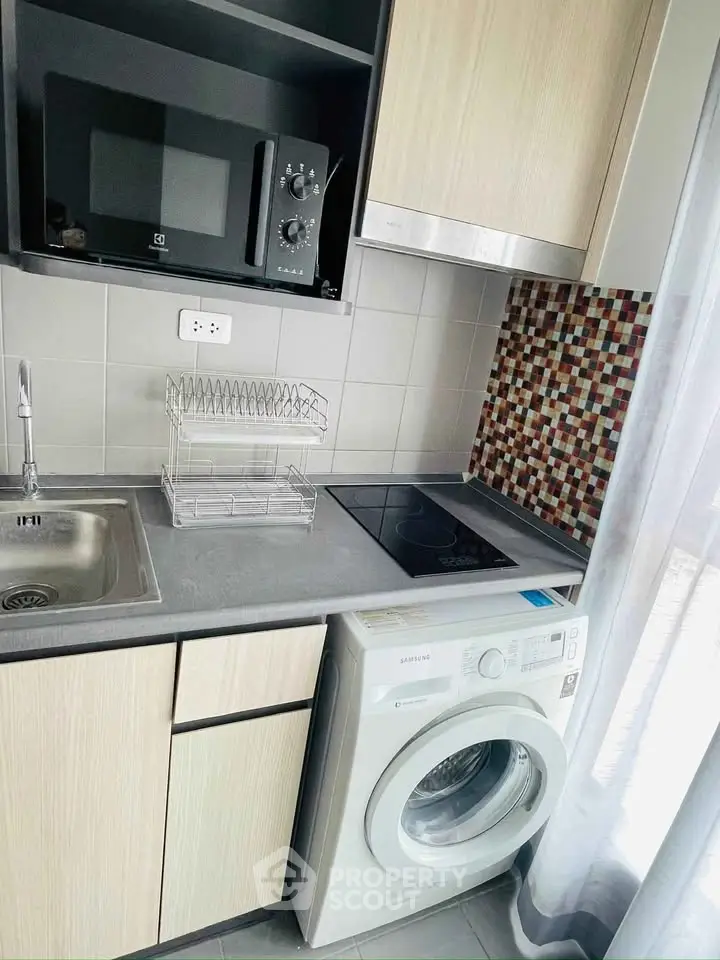 Modern kitchen with washing machine, microwave, and sleek cabinetry.