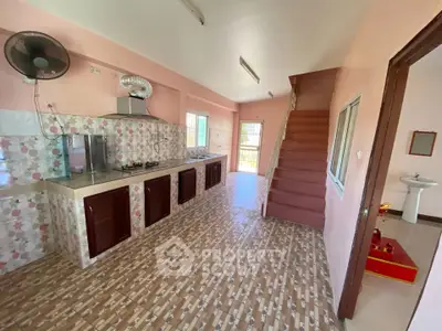 Spacious kitchen with open layout and staircase, featuring tiled flooring and modern gas stove.