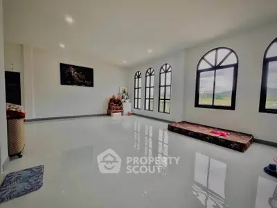 Spacious living room with large arched windows and glossy tiled floor, offering ample natural light and serene views.