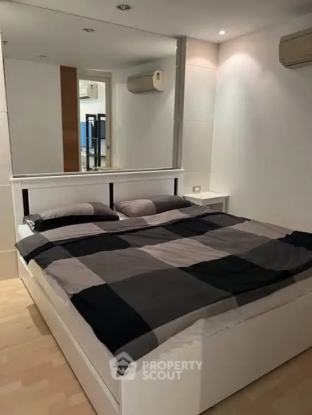 Modern bedroom with stylish decor and mirrored wall, featuring a comfortable double bed and sleek air conditioning units.