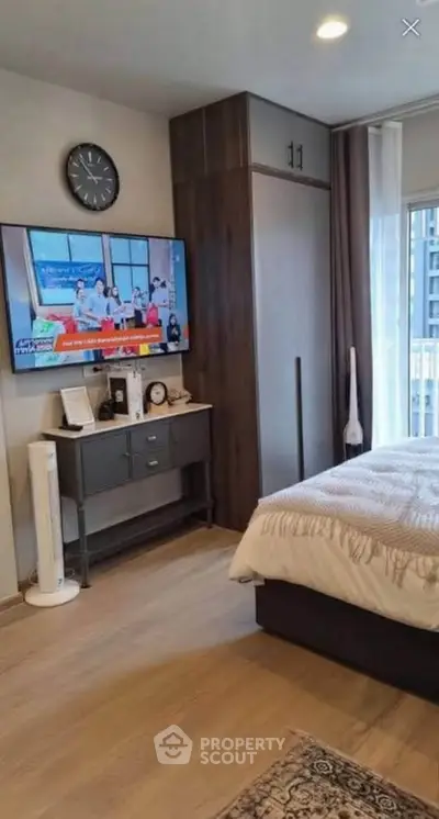 Modern bedroom with stylish decor, wall-mounted TV, and large window offering natural light.