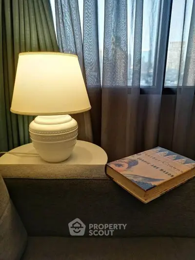 Cozy living room corner with elegant lamp and book on sofa by window.