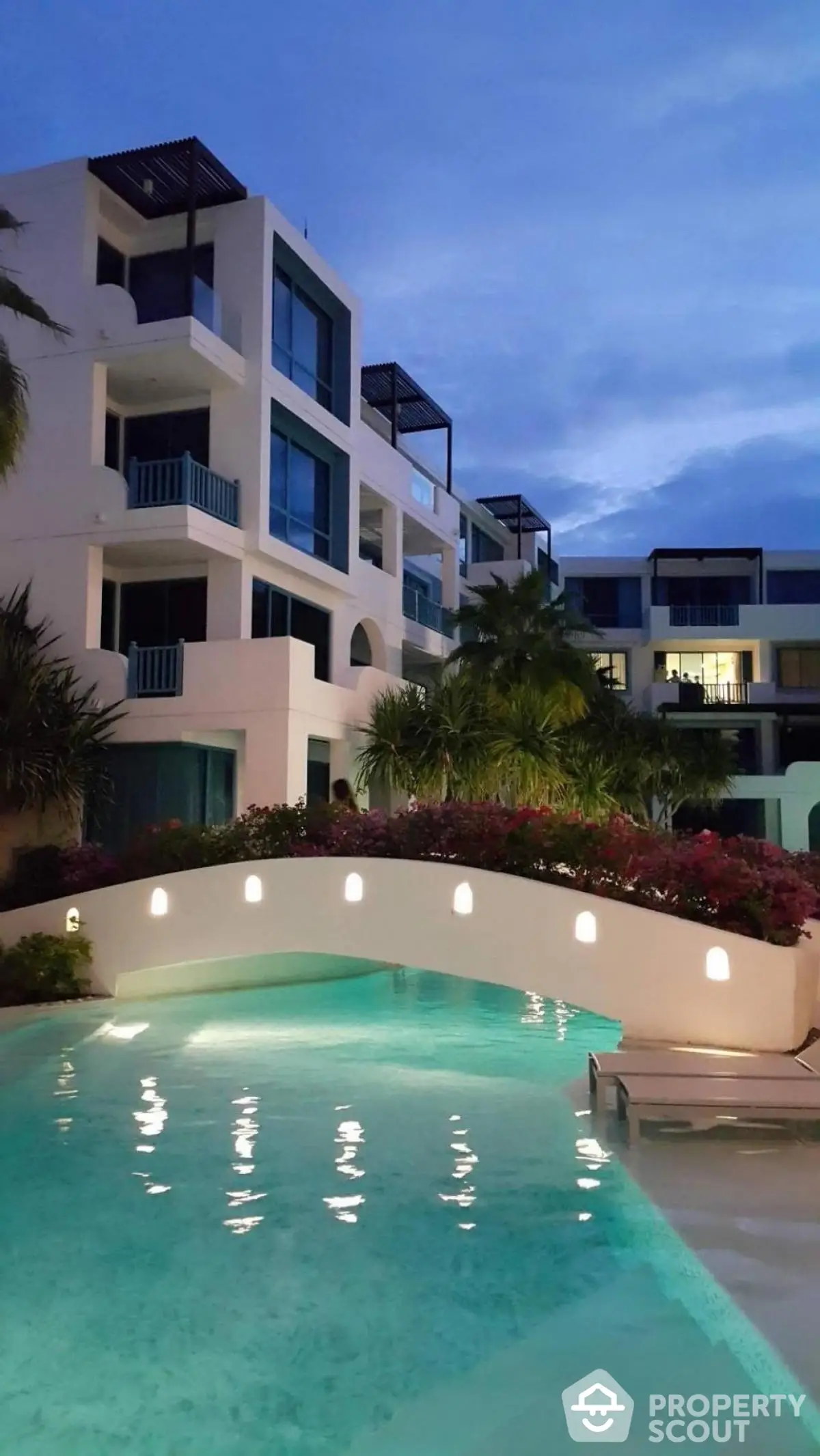 Luxurious modern apartment complex with stunning pool and lush landscaping at dusk.