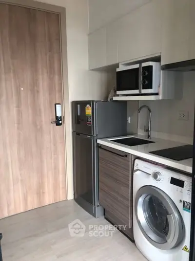 Modern compact kitchen with appliances including fridge, microwave, and washing machine.