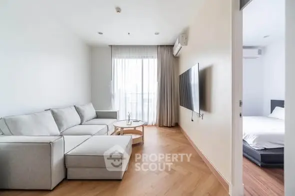 Modern living room with cozy sectional sofa and wall-mounted TV, adjacent to a bright bedroom.
