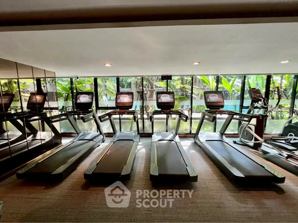Modern gym with multiple treadmills and large windows overlooking greenery.