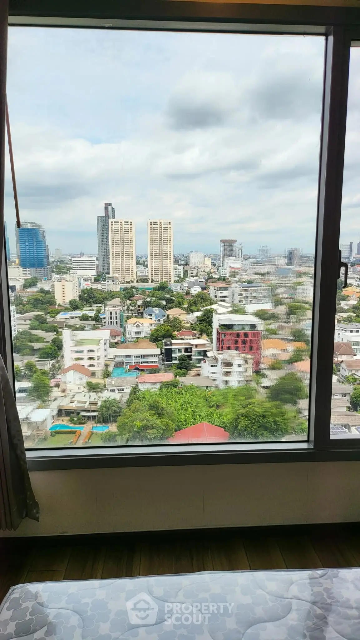 Stunning cityscape view from high-rise apartment window, showcasing urban skyline and lush greenery.