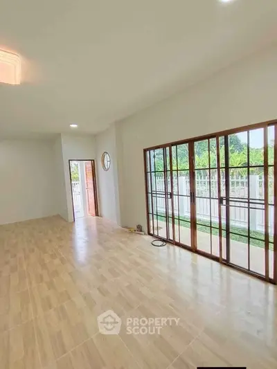 Spacious living room with large windows and garden view, featuring elegant wooden flooring.