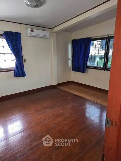 Spacious empty room with wooden flooring and blue curtains, perfect for customization.