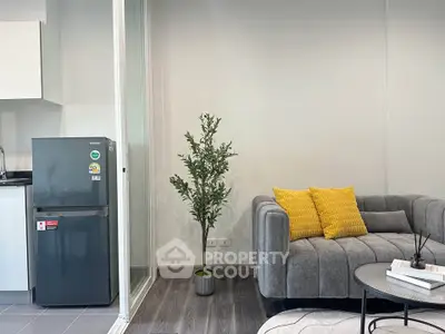Modern living room with stylish sofa, vibrant yellow cushions, and sleek kitchen area with compact fridge.