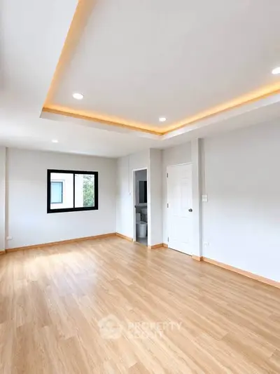 Spacious empty room with wooden flooring and modern recessed lighting, perfect for customization.