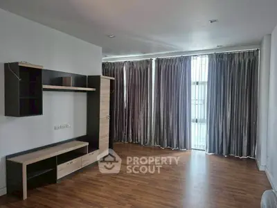 Spacious unfurnished living room with wooden flooring and large windows with curtains.