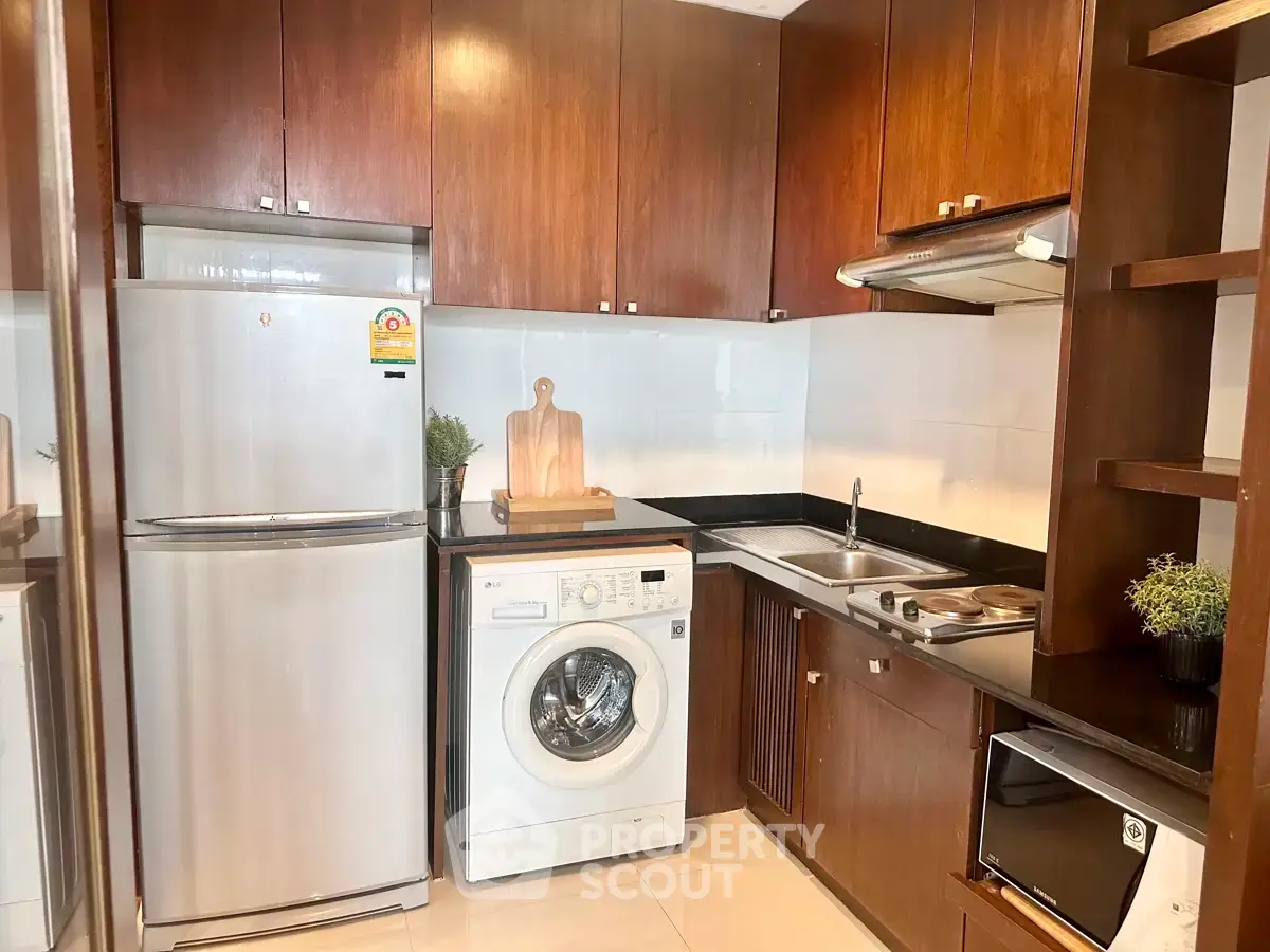 Modern kitchen with wooden cabinets, stainless steel fridge, washing machine, and microwave.