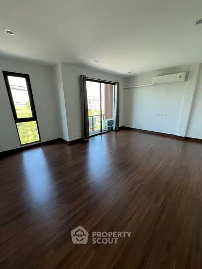 Spacious empty room with wooden flooring and large windows offering natural light.