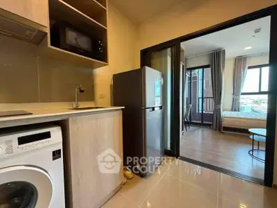 Modern apartment interior with kitchen and bedroom, featuring washing machine and fridge.