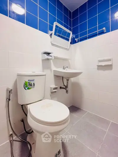 Compact bathroom with blue and white tiles, featuring a toilet and wall-mounted sink.