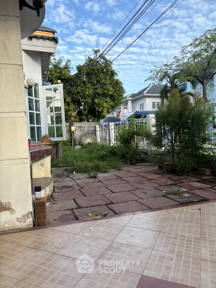 Charming residential outdoor area with tiled patio and lush greenery, perfect for relaxation and entertaining.