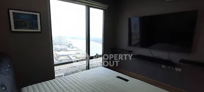 Modern bedroom with large window offering stunning city and river views, featuring a wall-mounted TV.
