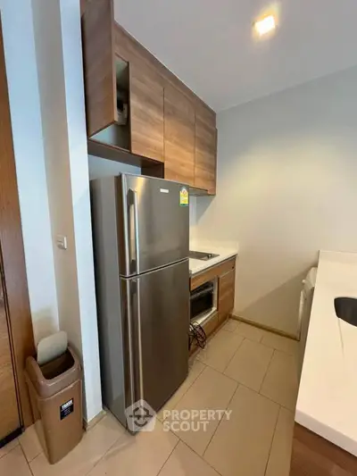 Modern kitchen with stainless steel fridge and wooden cabinets in compact layout.