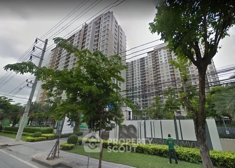 Modern high-rise residential building with lush greenery and street view.