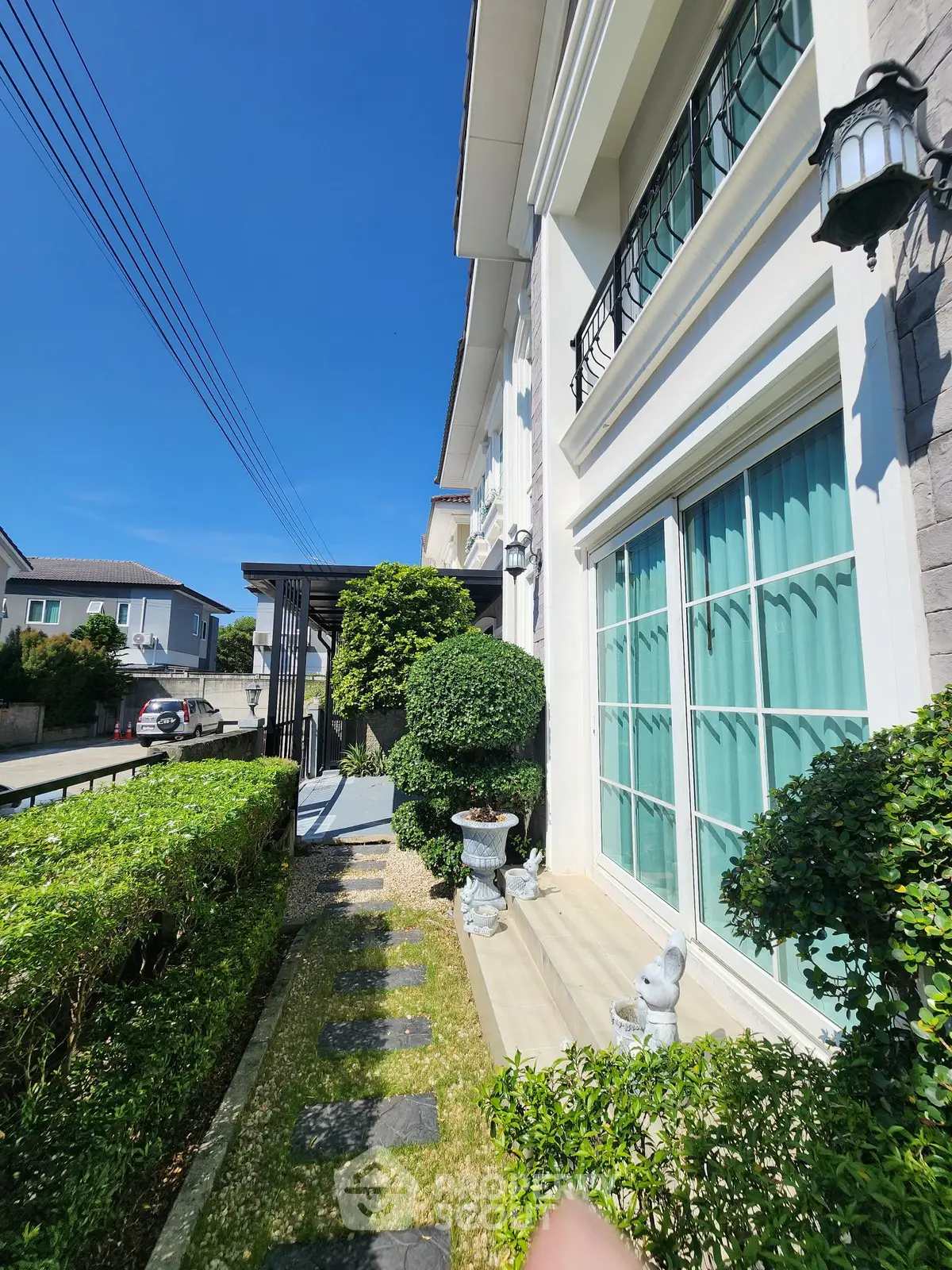 Charming residential exterior with lush greenery and elegant facade under clear blue sky.