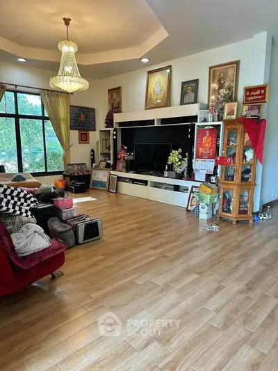 Spacious living room with elegant chandelier and wooden flooring, featuring a large entertainment center and cozy seating.